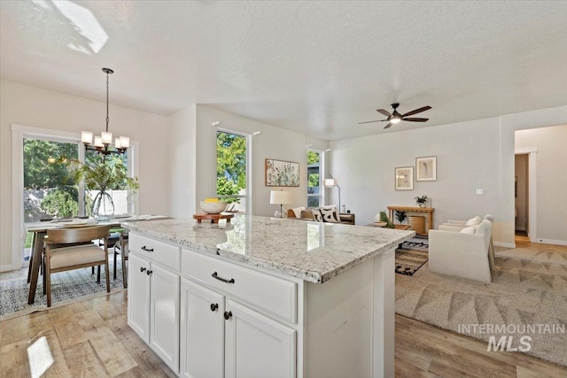 kitchen featuring pendant lighting, a center island, white cabinets, ceiling fan with notable chandelier, and a textured ceiling