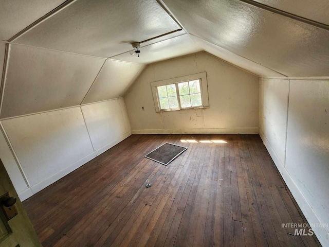 additional living space with a textured ceiling, lofted ceiling, and dark wood-type flooring