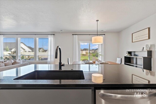 kitchen with a textured ceiling, a sink, dark countertops, open floor plan, and dishwasher