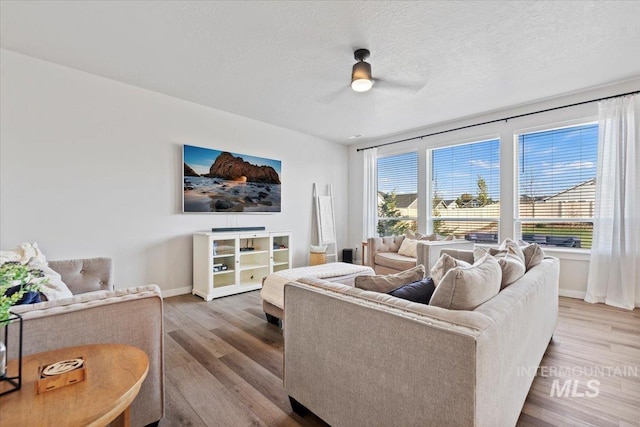 living room with a textured ceiling, ceiling fan, wood finished floors, and baseboards