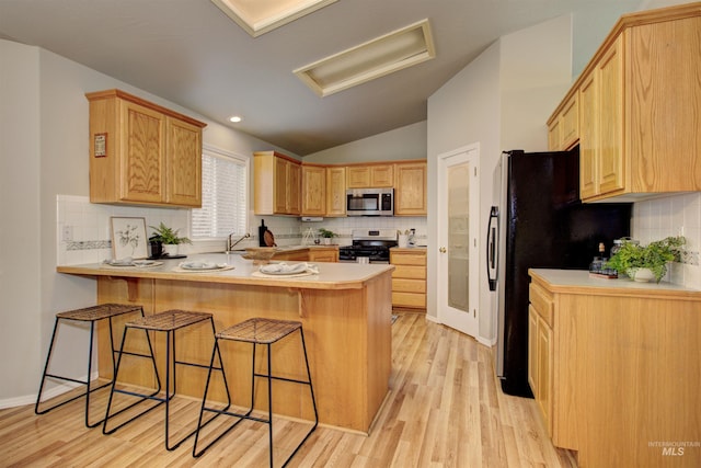 kitchen with a breakfast bar, a peninsula, lofted ceiling, appliances with stainless steel finishes, and light wood-type flooring