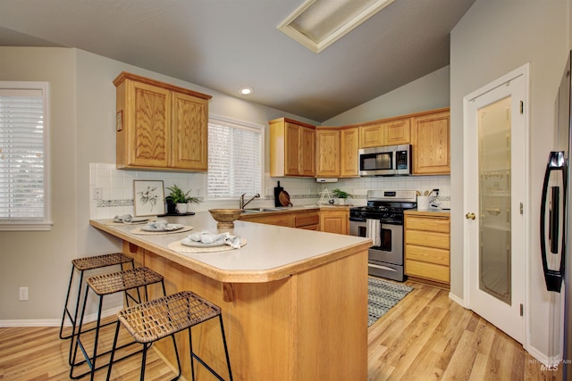 kitchen featuring a sink, stainless steel appliances, a peninsula, a breakfast bar area, and lofted ceiling