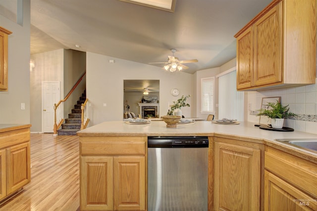 kitchen with a peninsula, a fireplace, light countertops, light wood-style floors, and dishwasher