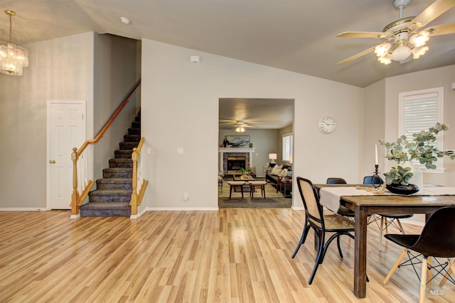 dining area with stairway, vaulted ceiling, ceiling fan with notable chandelier, a fireplace, and light wood-style flooring