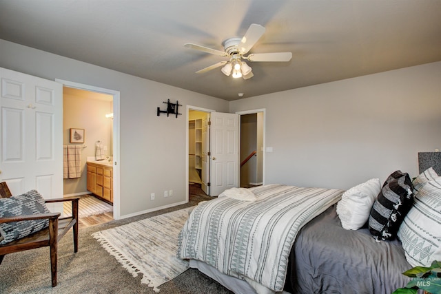 bedroom featuring light wood-type flooring, a walk in closet, ensuite bath, baseboards, and ceiling fan