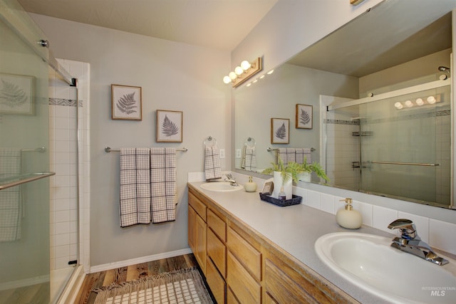 bathroom featuring double vanity, a stall shower, wood finished floors, and a sink