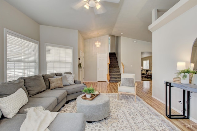 living area featuring light wood finished floors, baseboards, stairway, lofted ceiling, and ceiling fan with notable chandelier