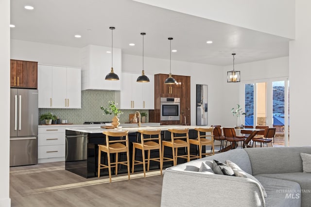 kitchen featuring white cabinetry, pendant lighting, backsplash, stainless steel fridge, and a kitchen island with sink