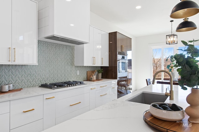 kitchen with wall chimney range hood, decorative backsplash, white cabinets, appliances with stainless steel finishes, and sink