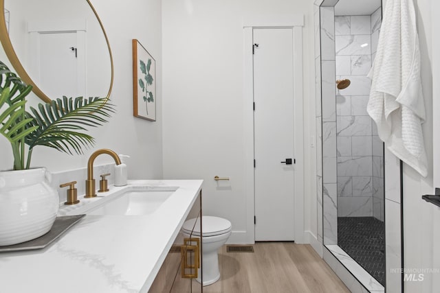 bathroom with a tile shower, vanity, toilet, and hardwood / wood-style floors