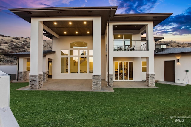 back house at dusk featuring a patio area and a yard