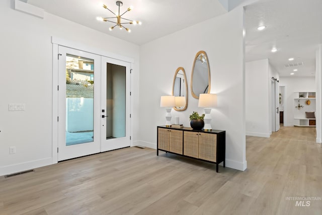 foyer with a notable chandelier, french doors, a barn door, and light hardwood / wood-style floors