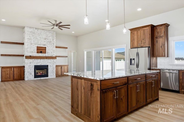 3119 Crescent Moon Rd, Twin Falls, ID 83301 - kitchen featuring appliances with stainless steel finishes, ceiling fan, light wood-style flooring, light stone countertops, and a fireplace