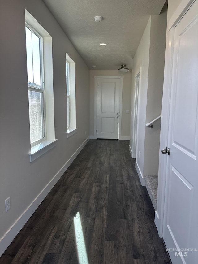 corridor featuring dark wood finished floors, a textured ceiling, and baseboards