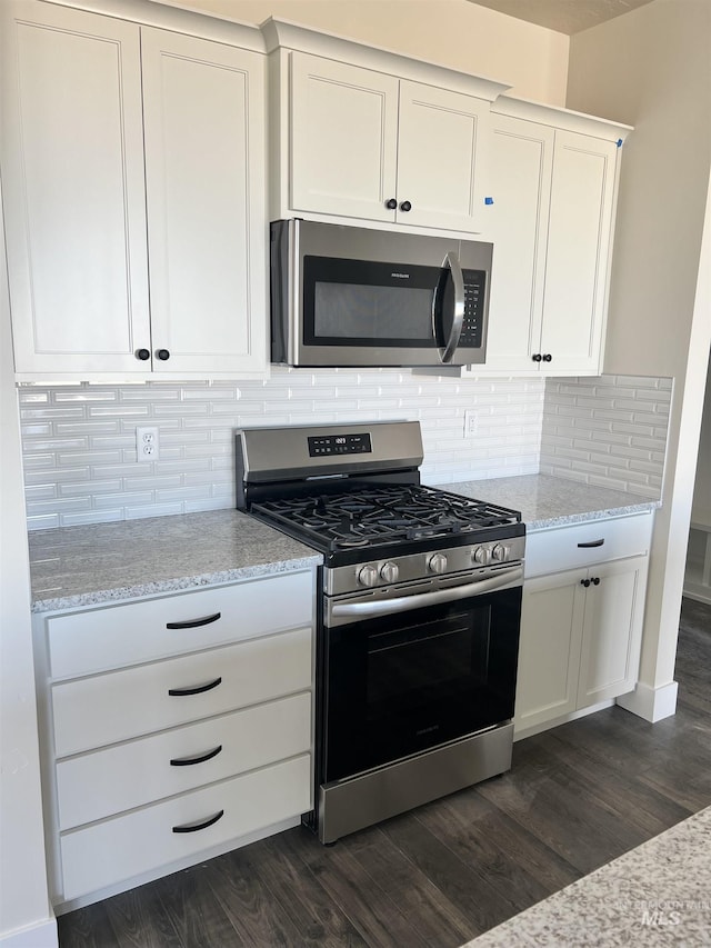 kitchen featuring dark wood-style floors, appliances with stainless steel finishes, light stone counters, white cabinetry, and backsplash