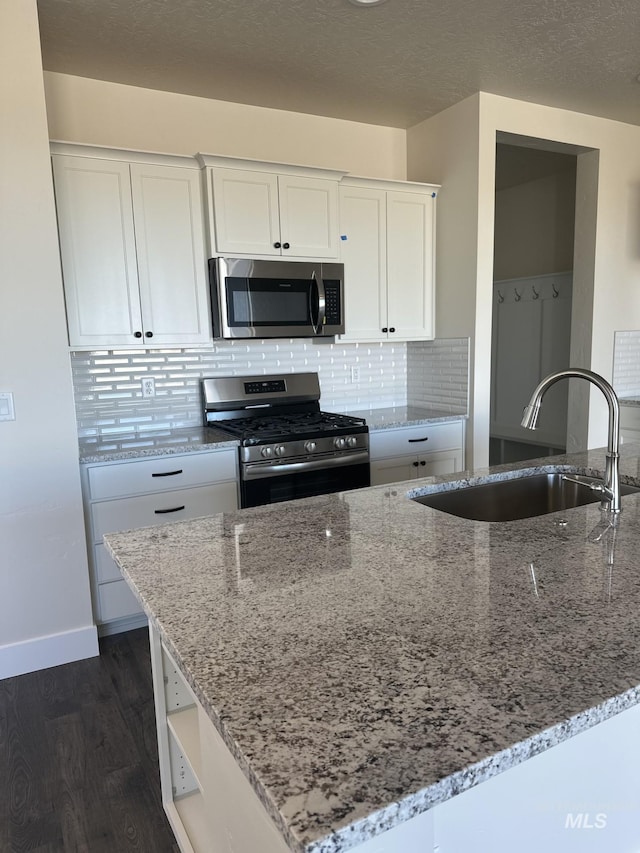 kitchen with sink, stainless steel appliances, light stone counters, dark hardwood / wood-style flooring, and white cabinets