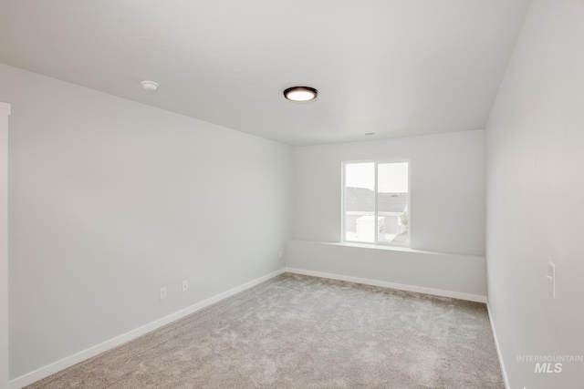 spare room featuring light carpet and baseboards