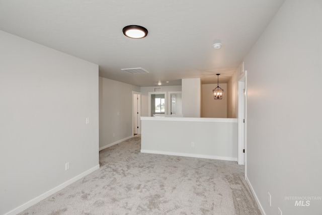 empty room featuring light carpet, visible vents, baseboards, and a chandelier