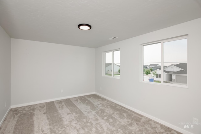 empty room featuring light carpet, a textured ceiling, visible vents, and baseboards