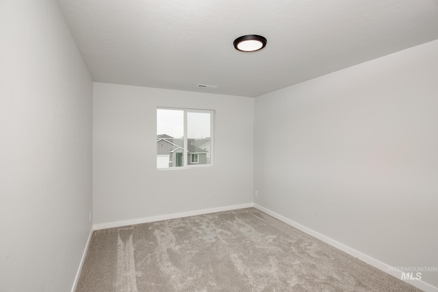 spare room featuring light colored carpet and baseboards