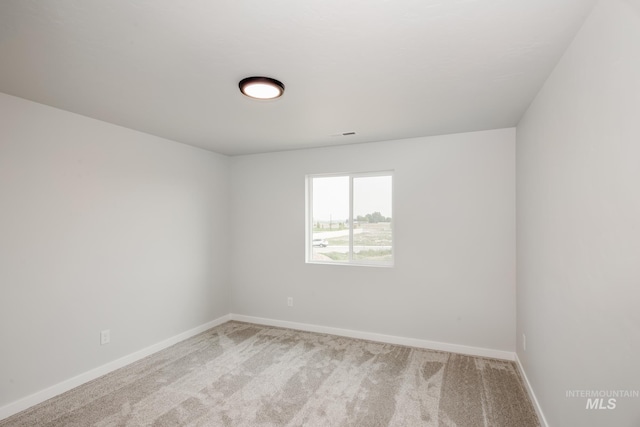 spare room featuring light carpet and baseboards