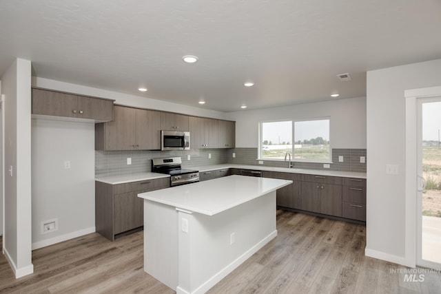 kitchen with a center island, stainless steel appliances, light countertops, light wood-type flooring, and a sink