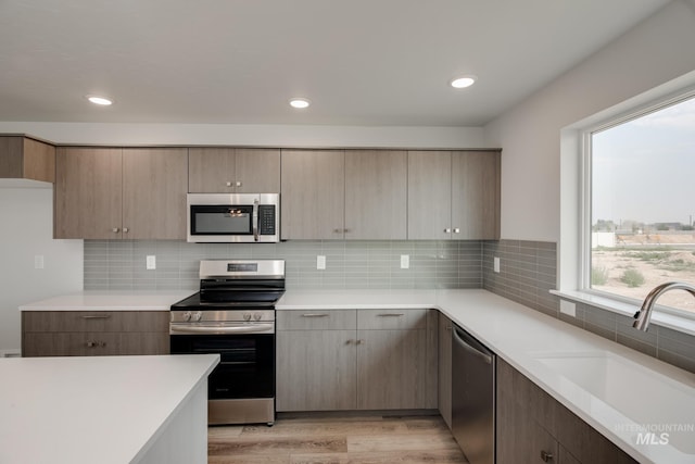 kitchen with light wood finished floors, light countertops, backsplash, appliances with stainless steel finishes, and a sink