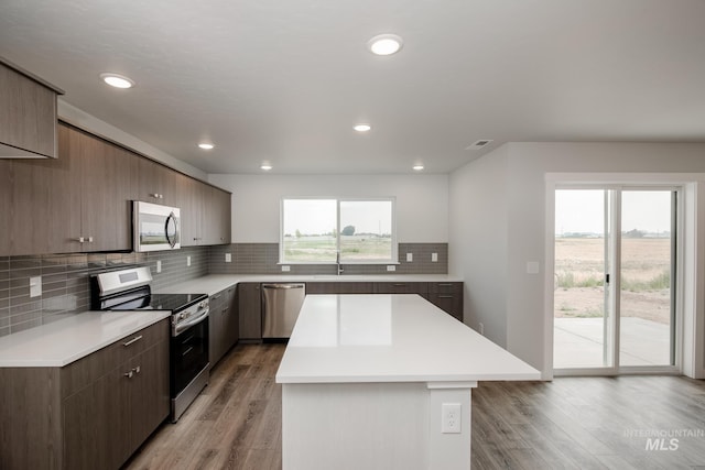 kitchen with a center island, tasteful backsplash, light countertops, appliances with stainless steel finishes, and light wood-style floors