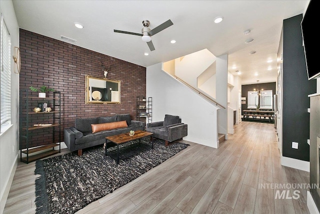 living room featuring visible vents, brick wall, wood finished floors, baseboards, and ceiling fan with notable chandelier