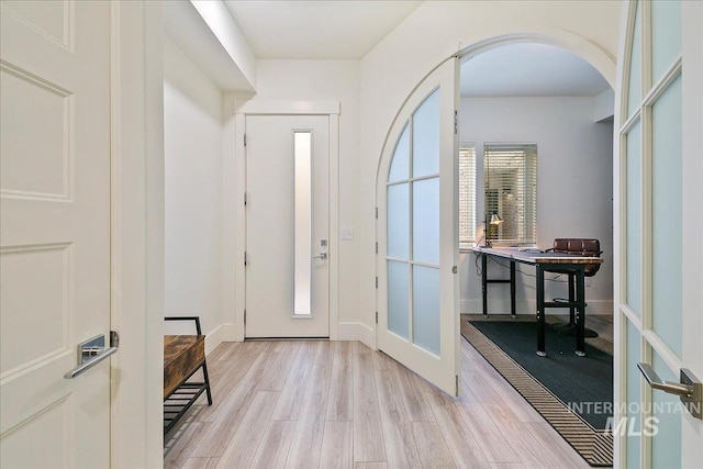 foyer with arched walkways, light wood-type flooring, and baseboards