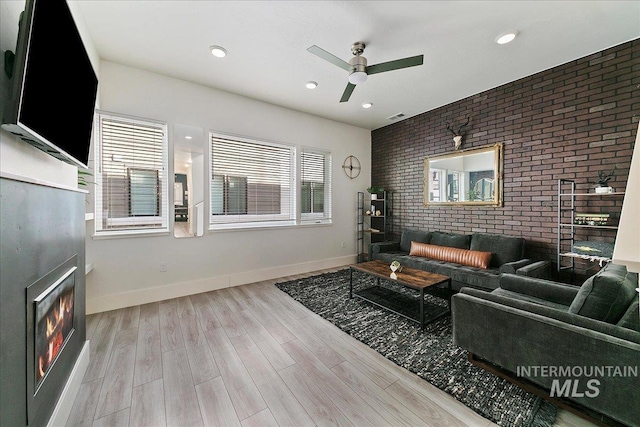 living area with visible vents, brick wall, wood finished floors, a warm lit fireplace, and baseboards