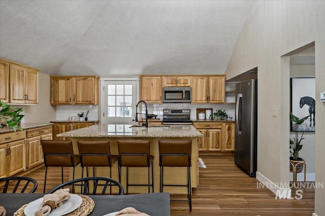 kitchen featuring an island with sink, light stone counters, backsplash, and stainless steel appliances