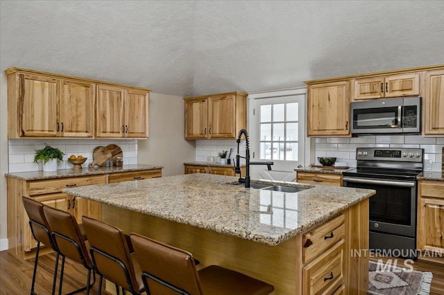 kitchen featuring dark wood-type flooring, sink, appliances with stainless steel finishes, and an island with sink