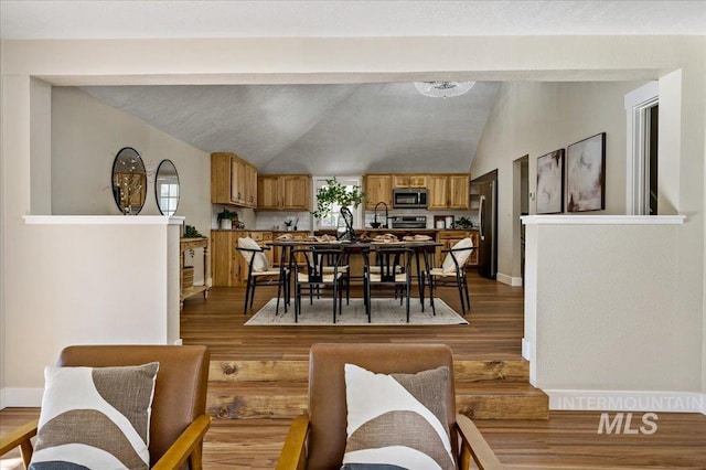 dining area featuring sink, hardwood / wood-style floors, and vaulted ceiling