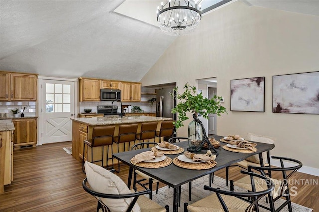 dining space with high vaulted ceiling, sink, dark hardwood / wood-style flooring, and an inviting chandelier