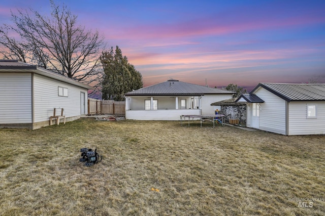 back of house featuring a yard, a trampoline, fence, and an outdoor structure