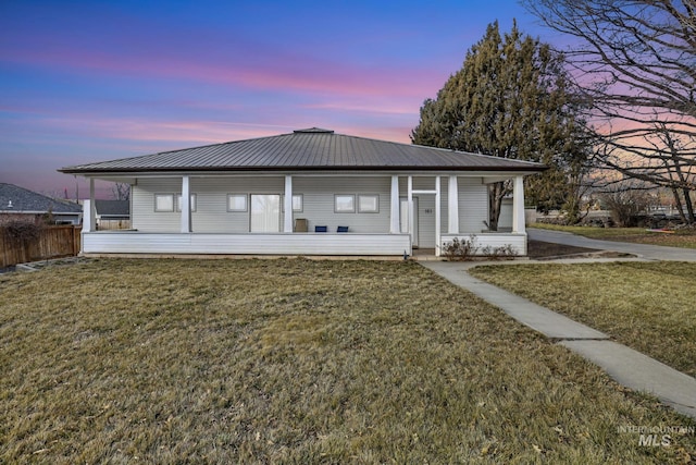 back of property at dusk featuring metal roof, covered porch, a lawn, and fence