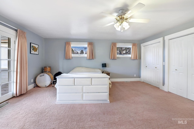 unfurnished bedroom featuring a ceiling fan, baseboards, two closets, and light colored carpet