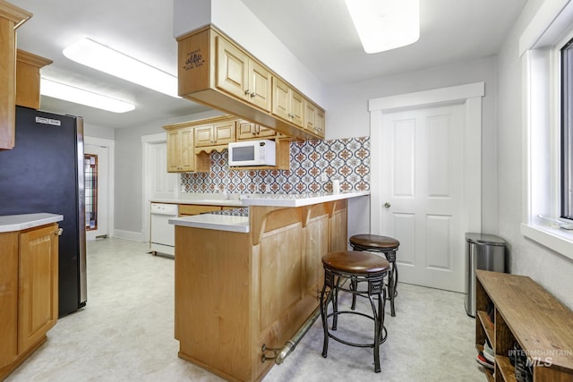 kitchen with light floors, light countertops, backsplash, white appliances, and a kitchen breakfast bar