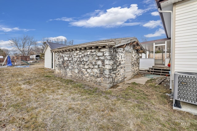 view of side of property with a lawn, stone siding, an outbuilding, central air condition unit, and a playground