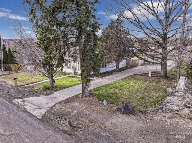 view of property hidden behind natural elements featuring a front yard, concrete driveway, and fence