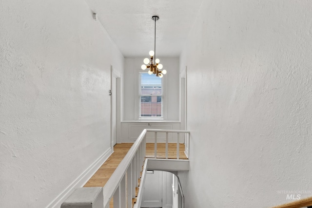 hallway featuring a notable chandelier and a textured wall