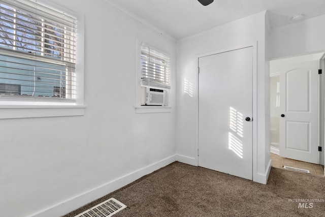 carpeted empty room with ornamental molding, cooling unit, visible vents, and baseboards