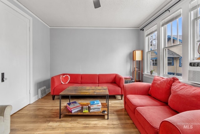 living room featuring ornamental molding, a ceiling fan, visible vents, and wood finished floors