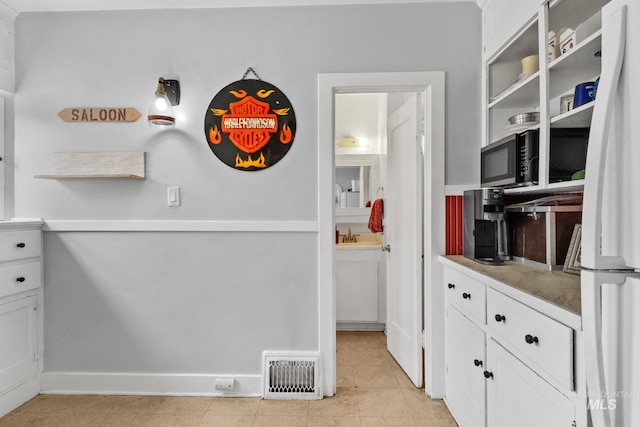 kitchen featuring light tile patterned floors, visible vents, freestanding refrigerator, light countertops, and white cabinetry