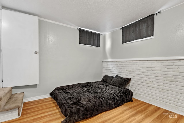 bedroom with baseboards, a textured ceiling, brick wall, and wood finished floors