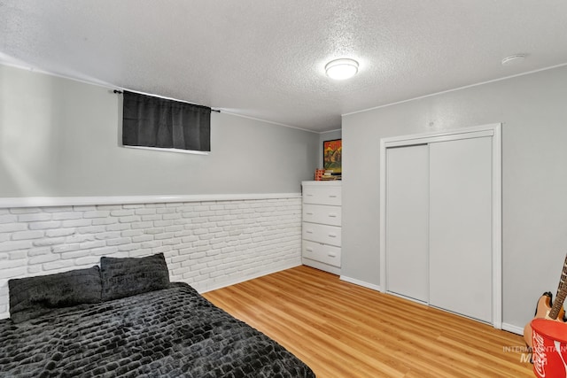 bedroom with a closet, brick wall, a textured ceiling, and light wood finished floors