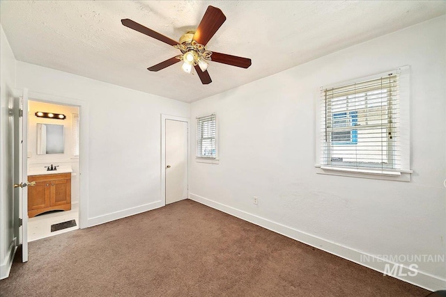 unfurnished bedroom featuring baseboards, connected bathroom, a textured ceiling, carpet flooring, and a sink