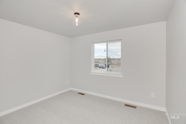empty room featuring baseboards, light carpet, and visible vents