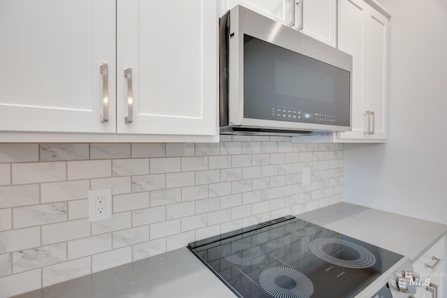 kitchen featuring white cabinetry, stainless steel microwave, stovetop, and backsplash